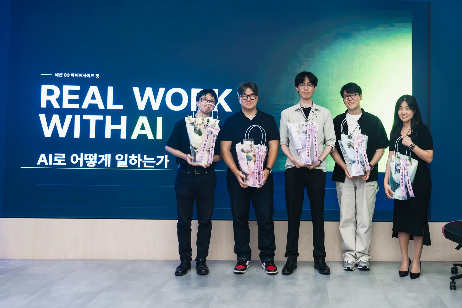 REAL WORK WITH AI 연사 5인이 행사 화면 앞에 선 무대
